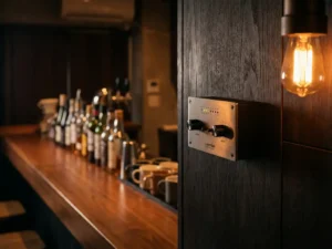 SPL-limiter op de muur van een café met warme amberverlichting, houten bar en wazige flessen op de achtergrond.
