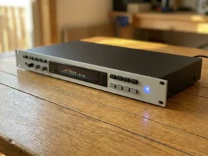 Zwarte 1U rack-unit met lichtgrijs frontpaneel op eiken houten oppervlak, met spectrumanalyzer en blauw LED-licht.