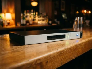Zwarte 1U rack-unit met lichtgrijze frontplaat op eiken oppervlak, blauwe LED-indicator en verlichte meterkolommen in een bar.